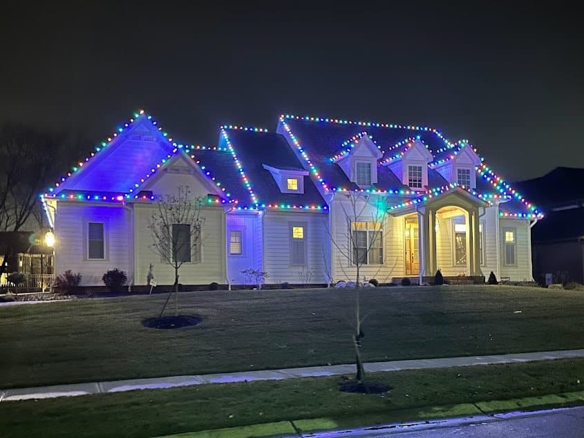 White ranch home with blue and multicolor Christmas lights outlining the roofline